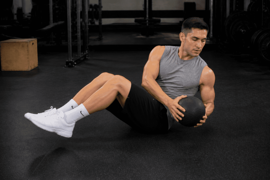 Man performing Russian twist with a medicine ball on a gym floor.